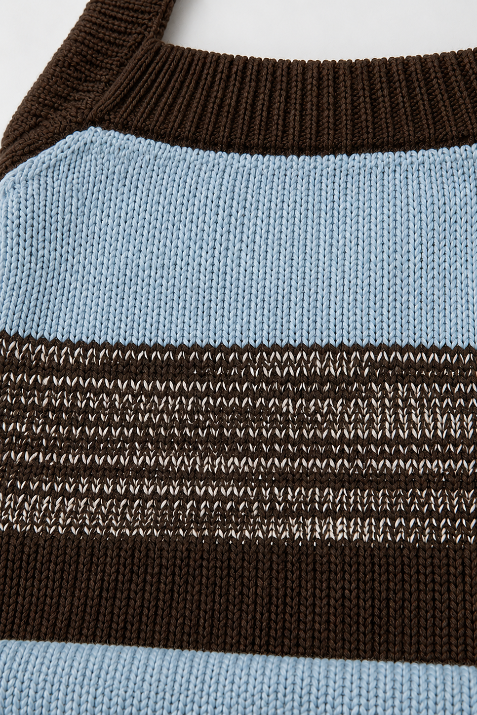 Close-up of a knitted striped sweater or bag with horizontal bands of light blue, dark brown, and a textured multicolor stripe in the middle.