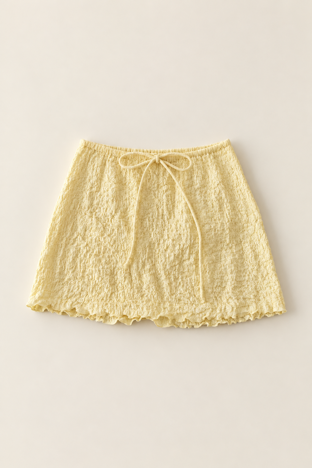 A pale yellow textured mini skirt with a drawstring waist, laid flat against a light beige background.