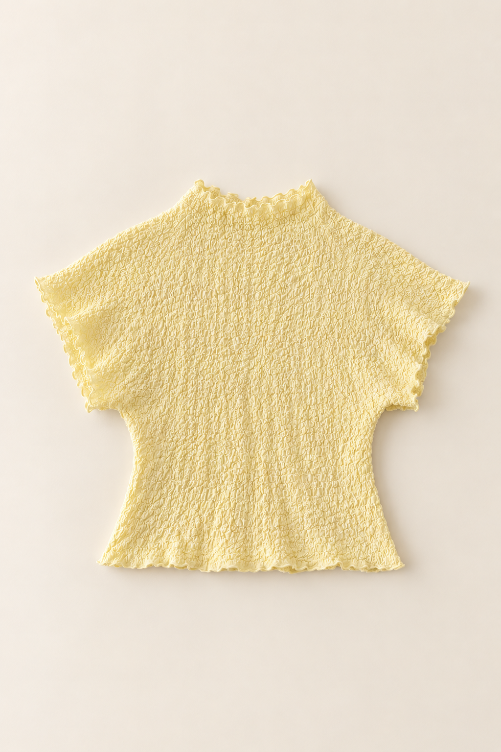A pale yellow short-sleeve top with a textured, crinkled fabric and scalloped edges, laid flat against a light beige background.
