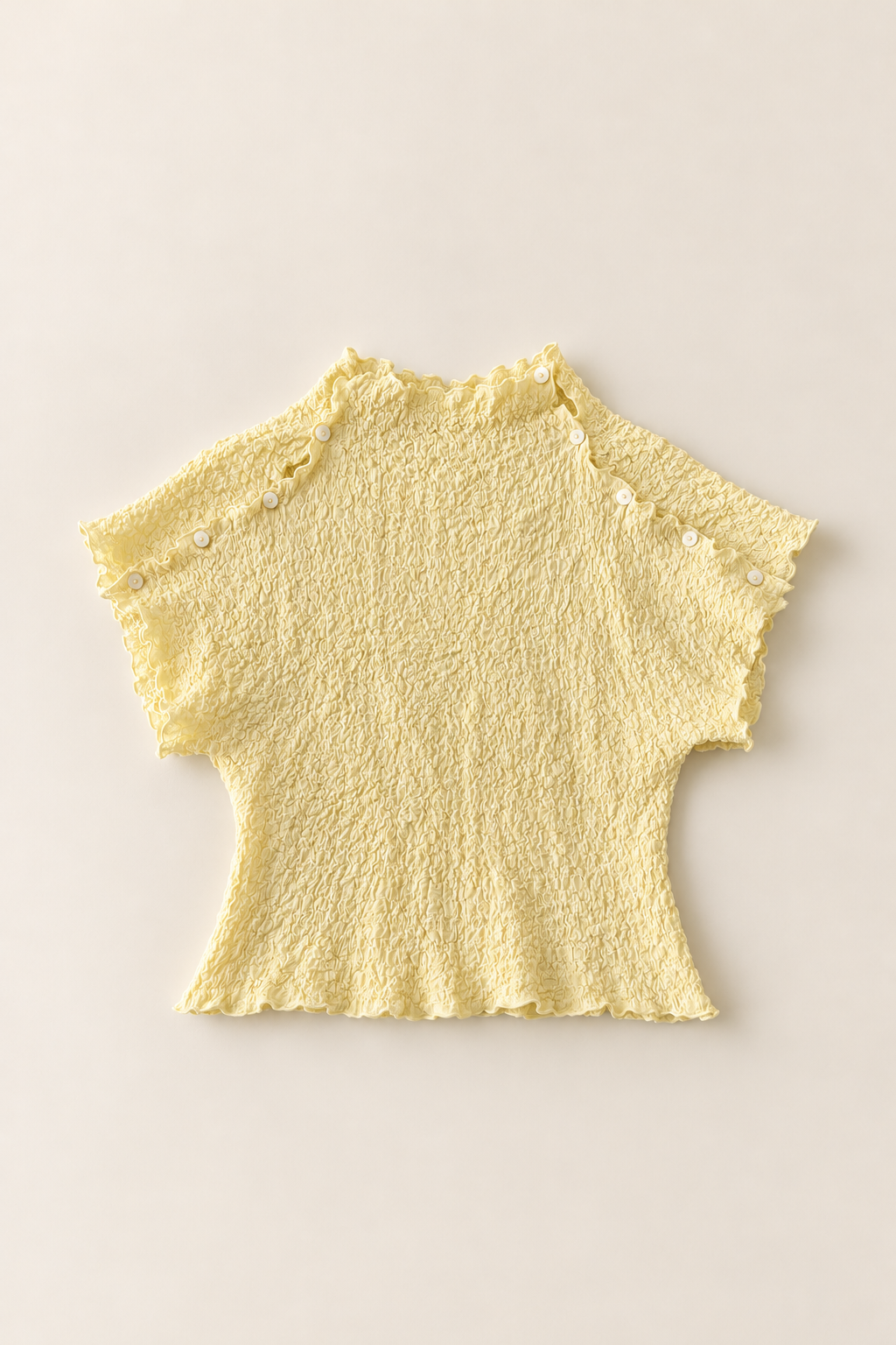 A pale yellow short-sleeve knit top with a textured, crinkled fabric, scalloped edges, and decorative buttons on the sleeve cuffs, laid flat against a light beige background.