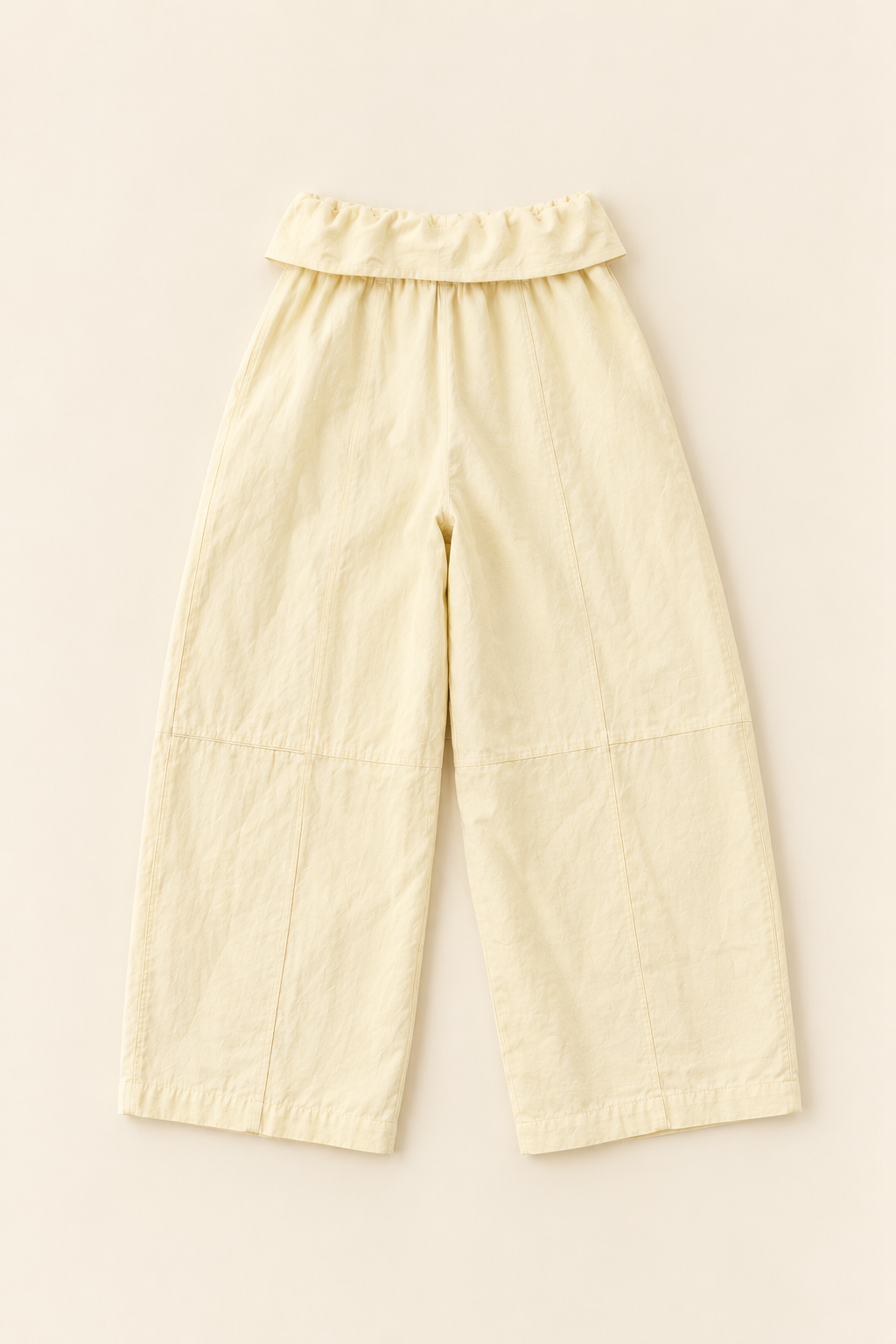 Cream-colored cropped pants with a ruffled waistband, laid flat on a light beige background.