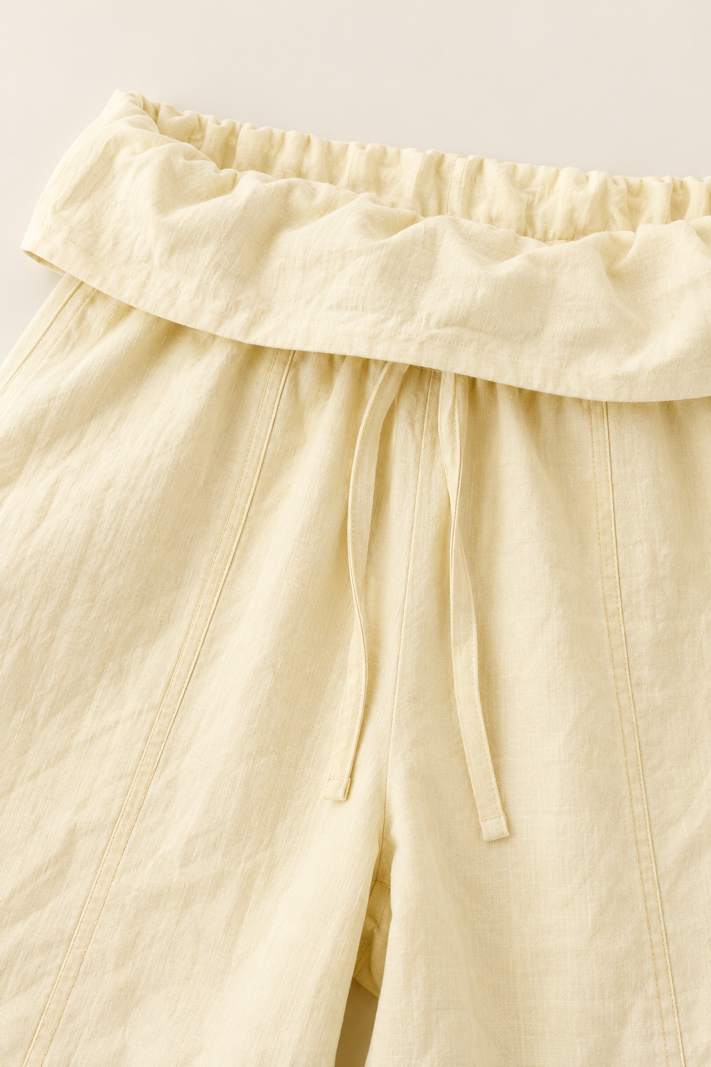 Close-up of a pair of light cream or pale yellow linen pants with an elasticized waistband and drawstring.