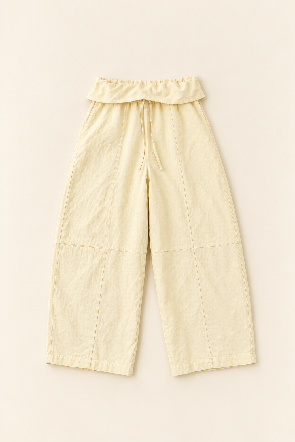 Linen soft yellow pants with a folded waistband and a drawstring. It has a horizontal seamline on the knee and a vertical seamline in the center of the legs. The pants has a soft barrel shape. 